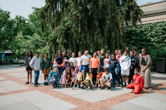 A group of students posing for a group photo in front of a tall tree at Longwood Gardens.